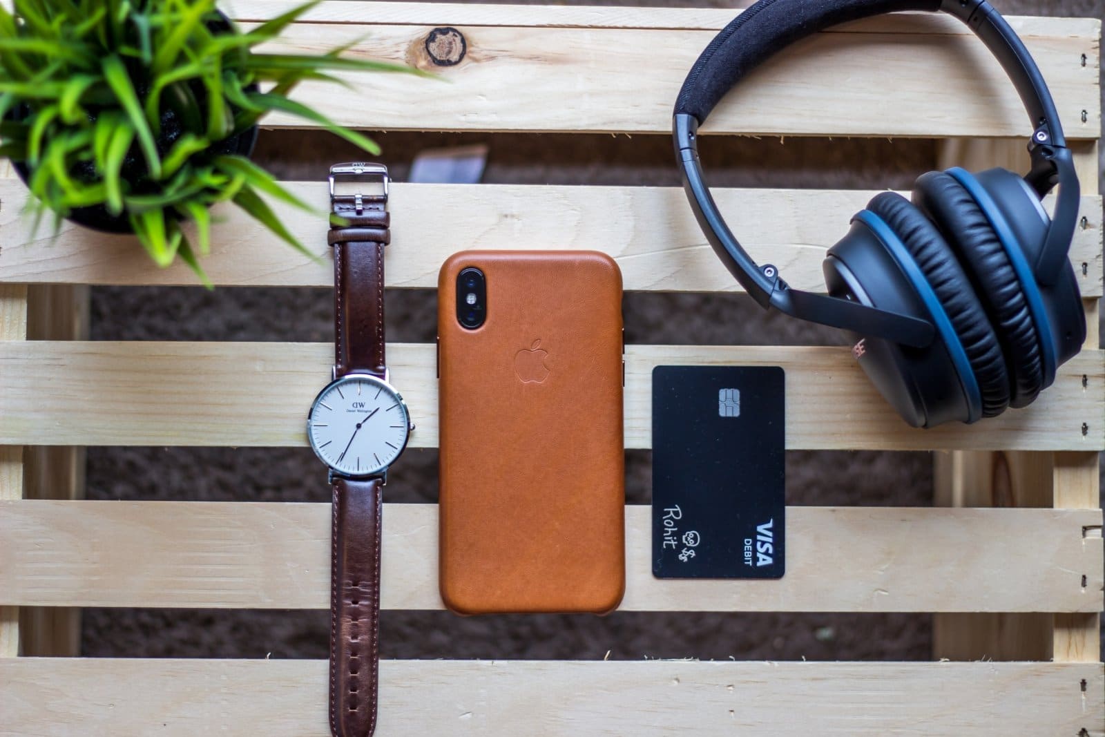 brown iPhone case beside round silver-colored analog watch on brown wooden table
