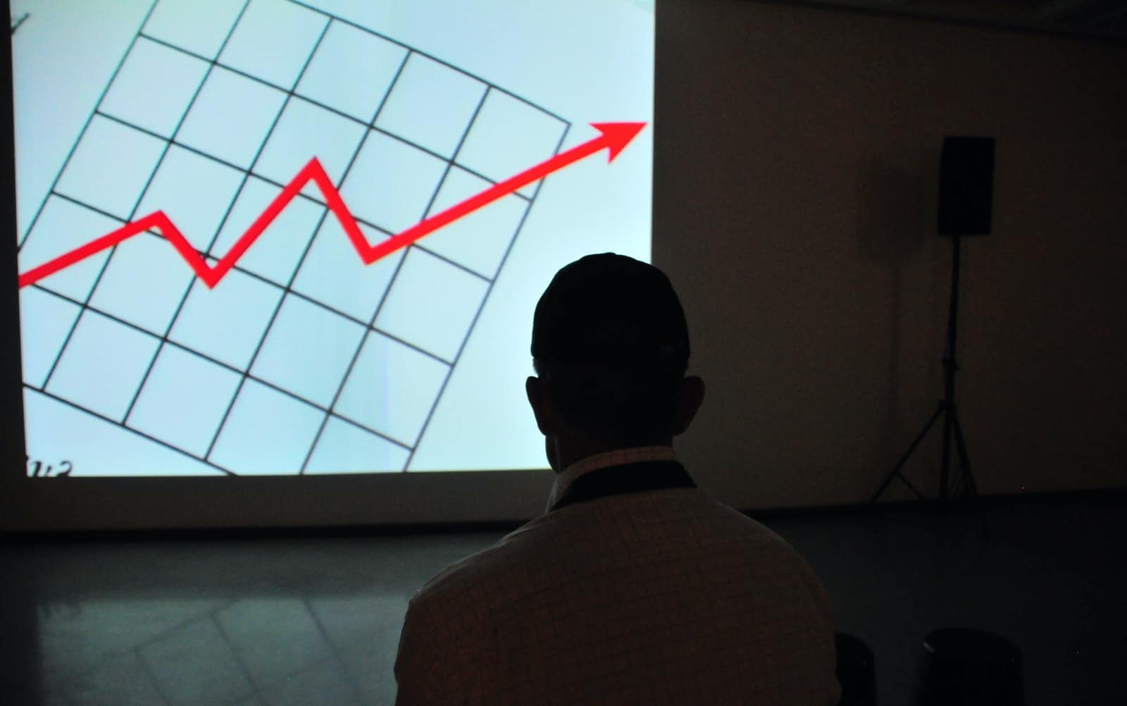 man wearing white top looking at projector graph screen
